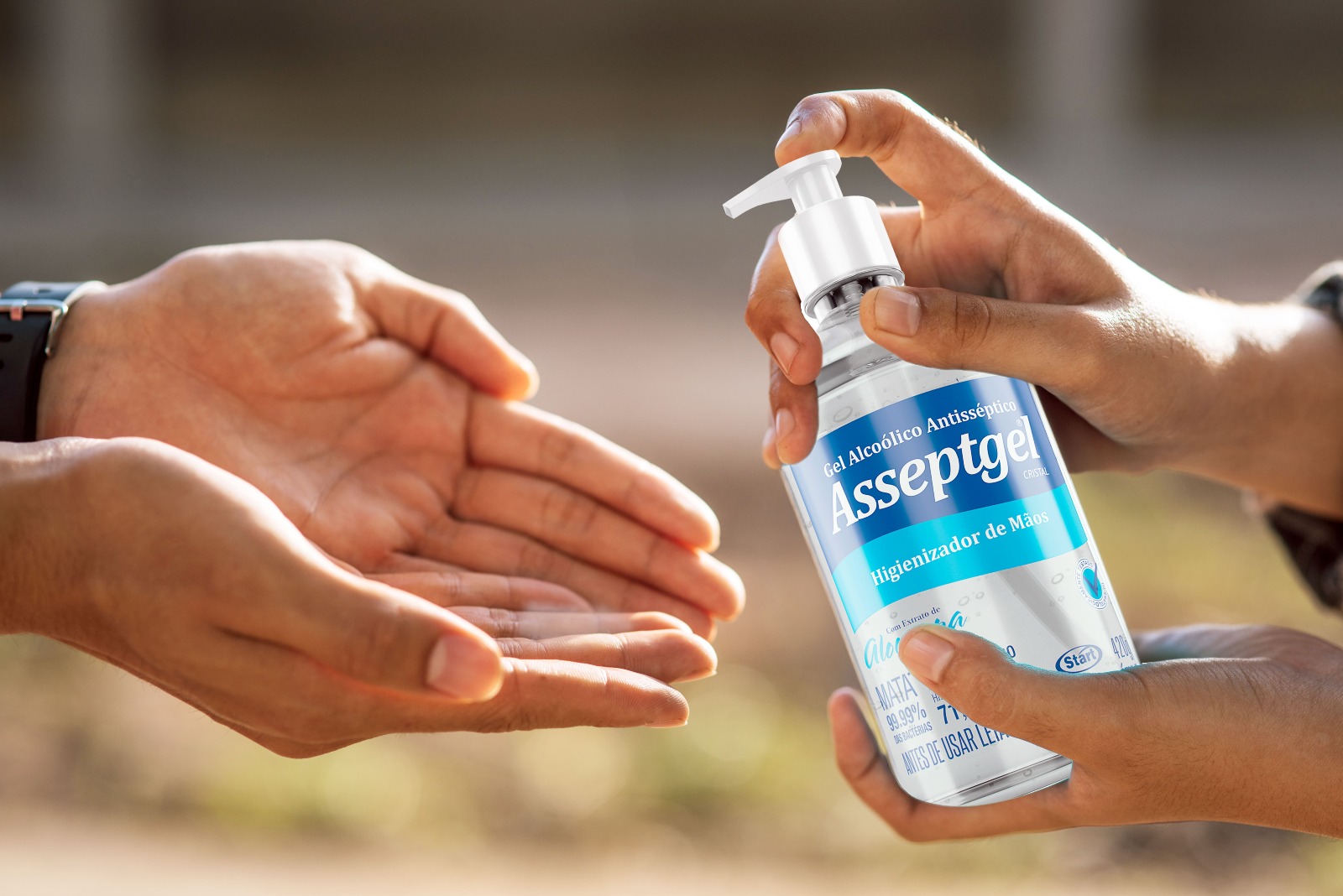 Pessoa aplicando álcool gel Asseptgel nas mãos de outra pessoa. 