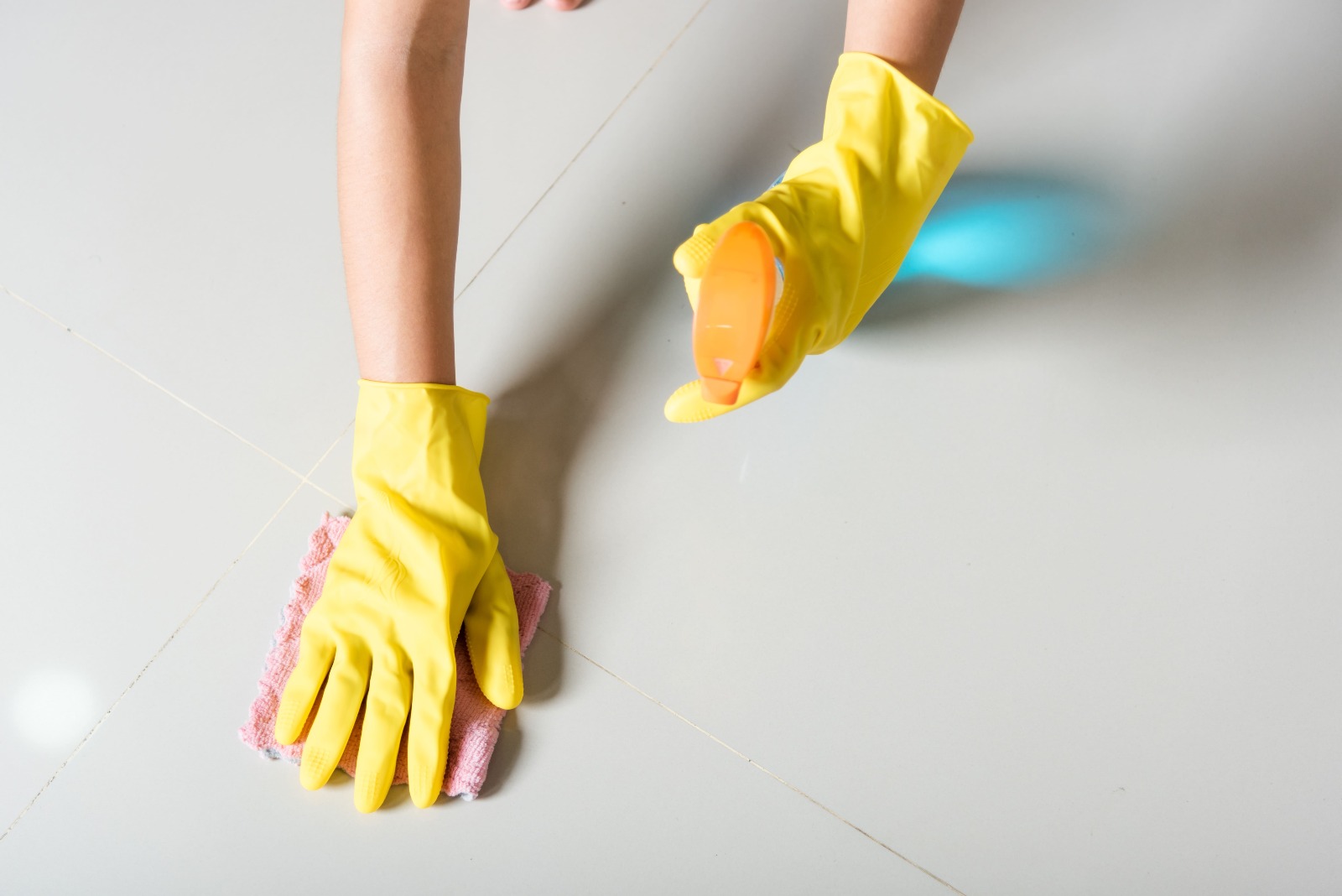  Pessoa usando luvas de borracha, pano e borrifador para limpar o piso de porcelanato.