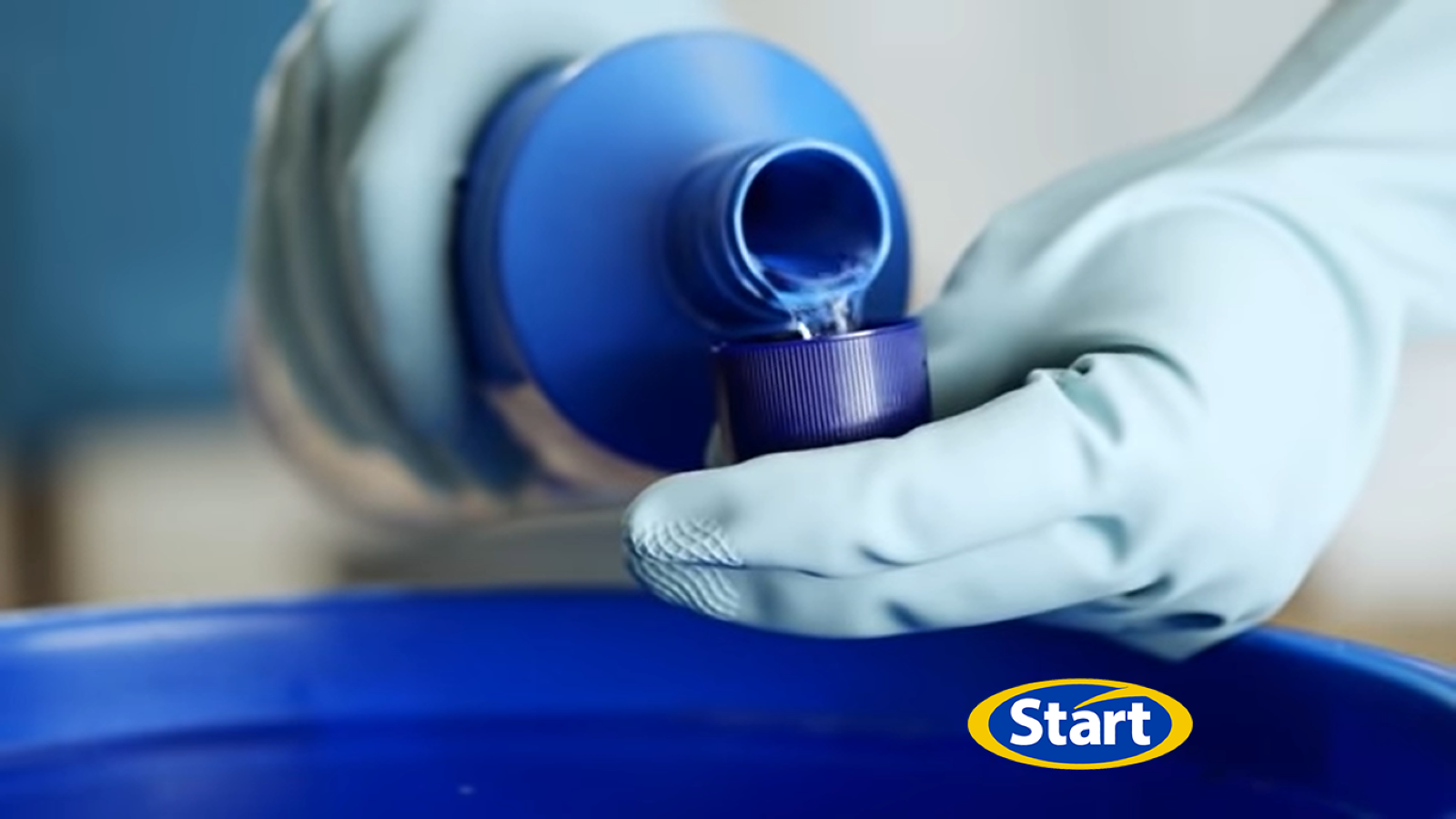 Foto de mãos com luvas segurando uma embalagem de Azulim. Uma segura o produto enquanto outra está mensurando a quantidade, colocando o produto na tampa. 